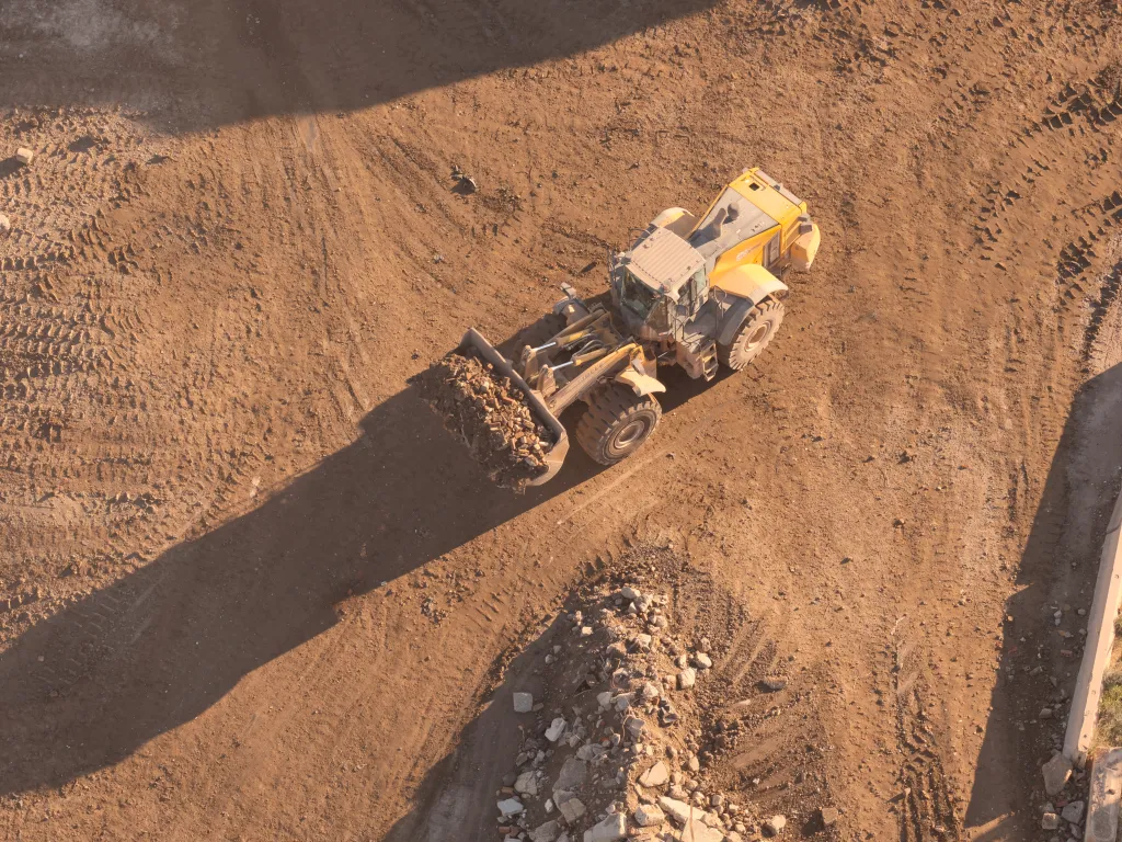 Aerial view of a construction site with a loader machinery moving dirt and debris on a sandy surface.
