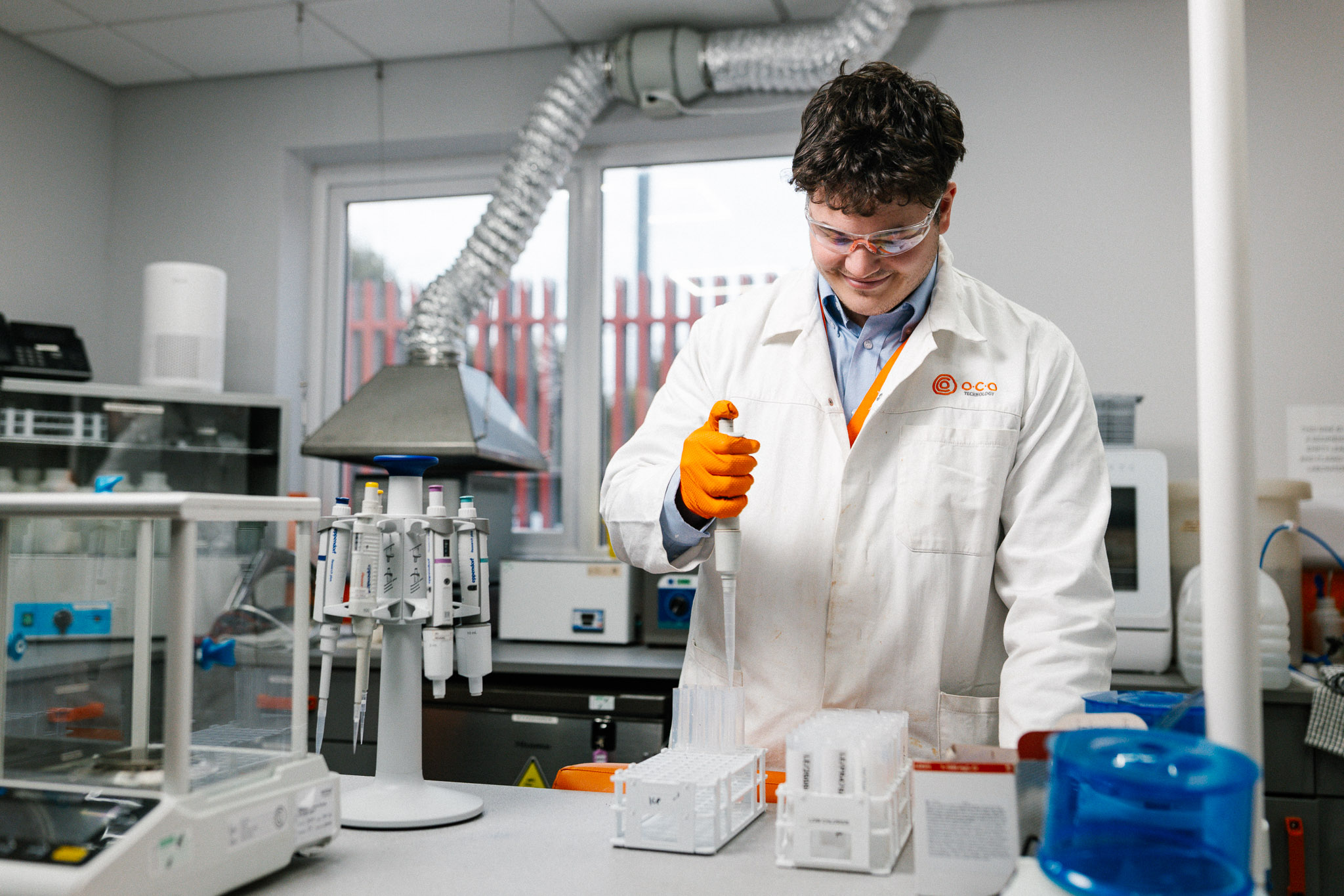 A scientist in a lab coat and safety goggles is using a pipette in a laboratory setting, as part of the development in carbon capture technology.